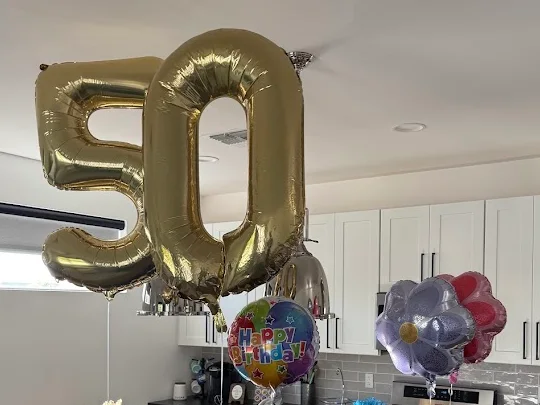 Gold number 50 balloons and birthday balloons floating above a kitchen island