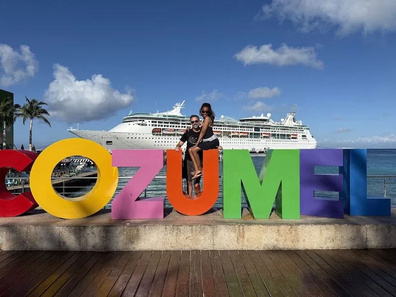 Patrick and Tamekia at the Cozumel sign, cruise ship docked behind them