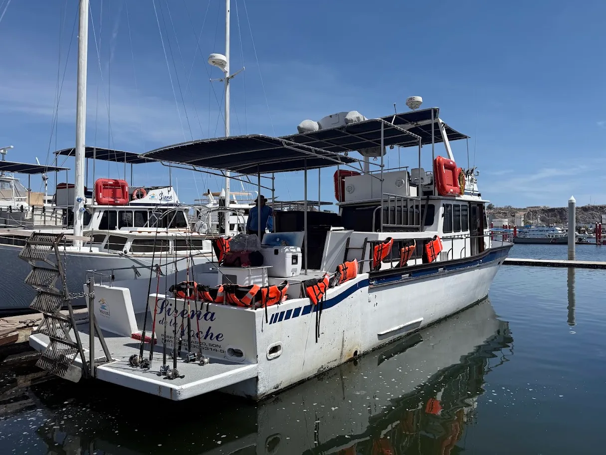 A fishing charter boat tied up at the dock in Puerto Peñasco, with fishing rods lined up at the stern and orange life jackets on the rail
