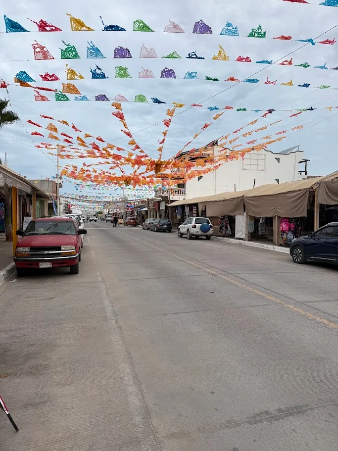 A shopping street in Puerto Peñasco with colorful papel picado strung overhead and shops and awnings along the sides