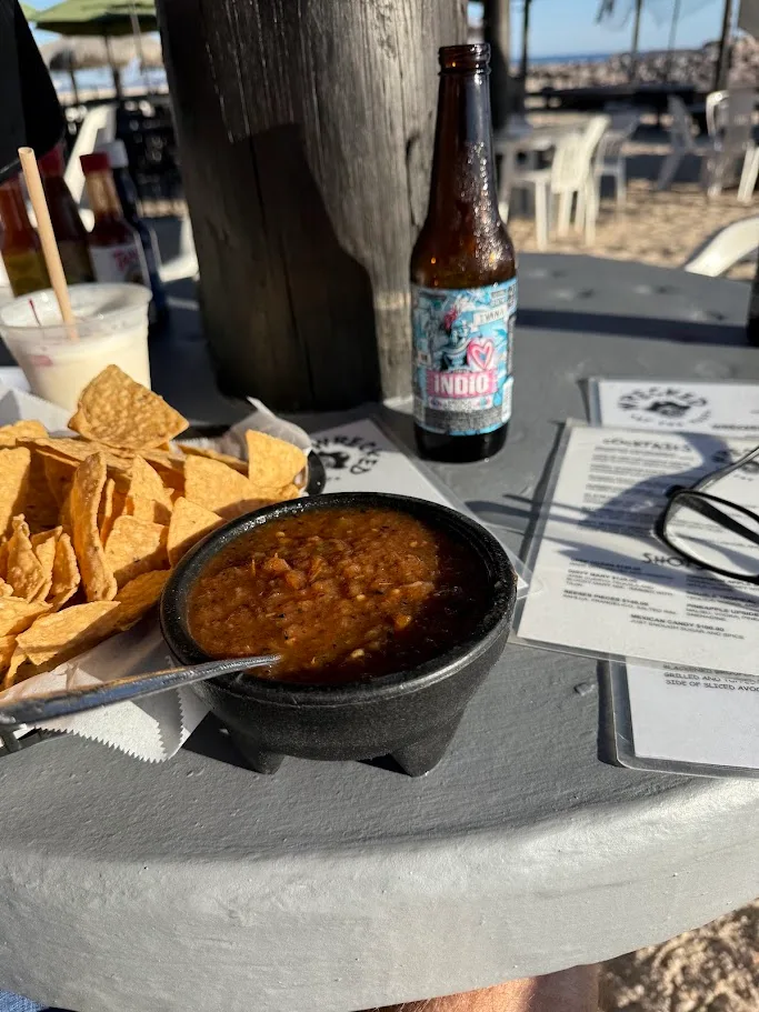A bowl of salsa, a basket of chips, and a cold Indio beer on a table at Wrecked, on the beach
