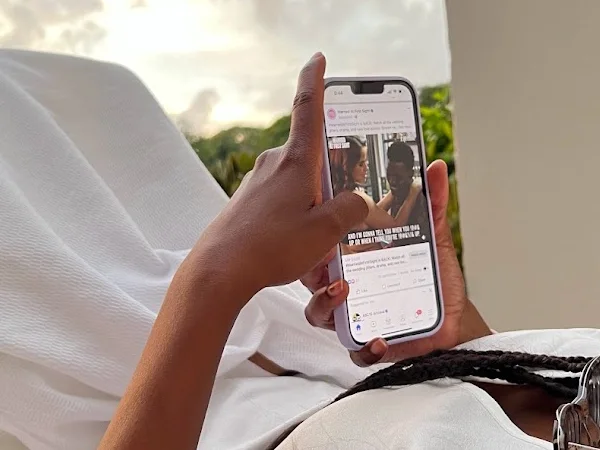 A hand holding a phone that shows a social media post, with a cloudy sunset sky behind it