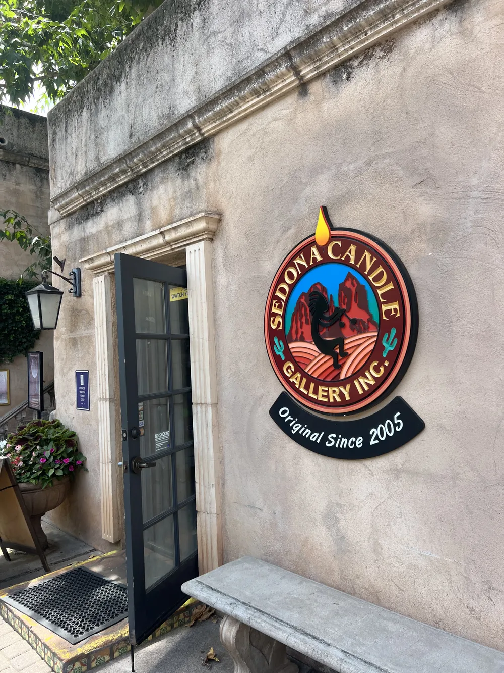 The Sedona Candle Gallery sign on an adobe wall at Tlaquepaque, with an open door and a stone bench