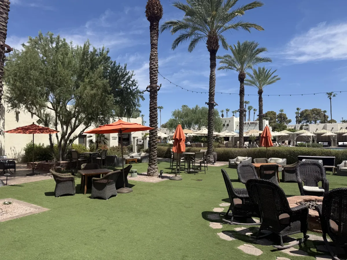A grassy lawn at The Wigwam with rocking chairs, fire pits, and string lights under tall palms